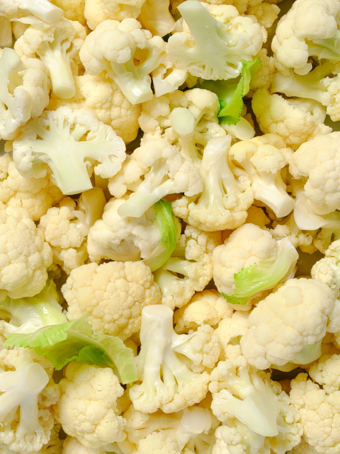 Close-up of raw cauliflower florets with a few small green leaves scattered throughout
