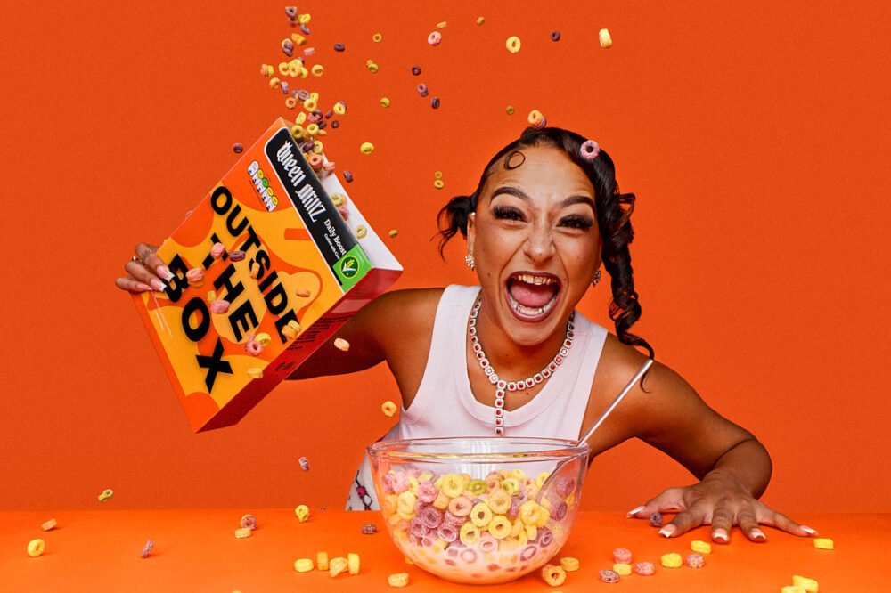 portrait of a rapper on a block colour orange set throwing fruit loop cereal