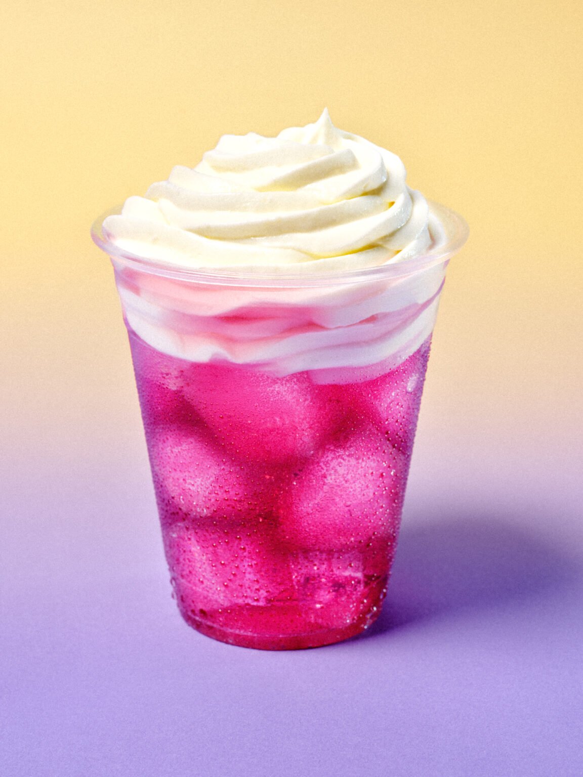 Iced pink berry drink over ice, topped with a swirl of whipped cream, in a clear cup