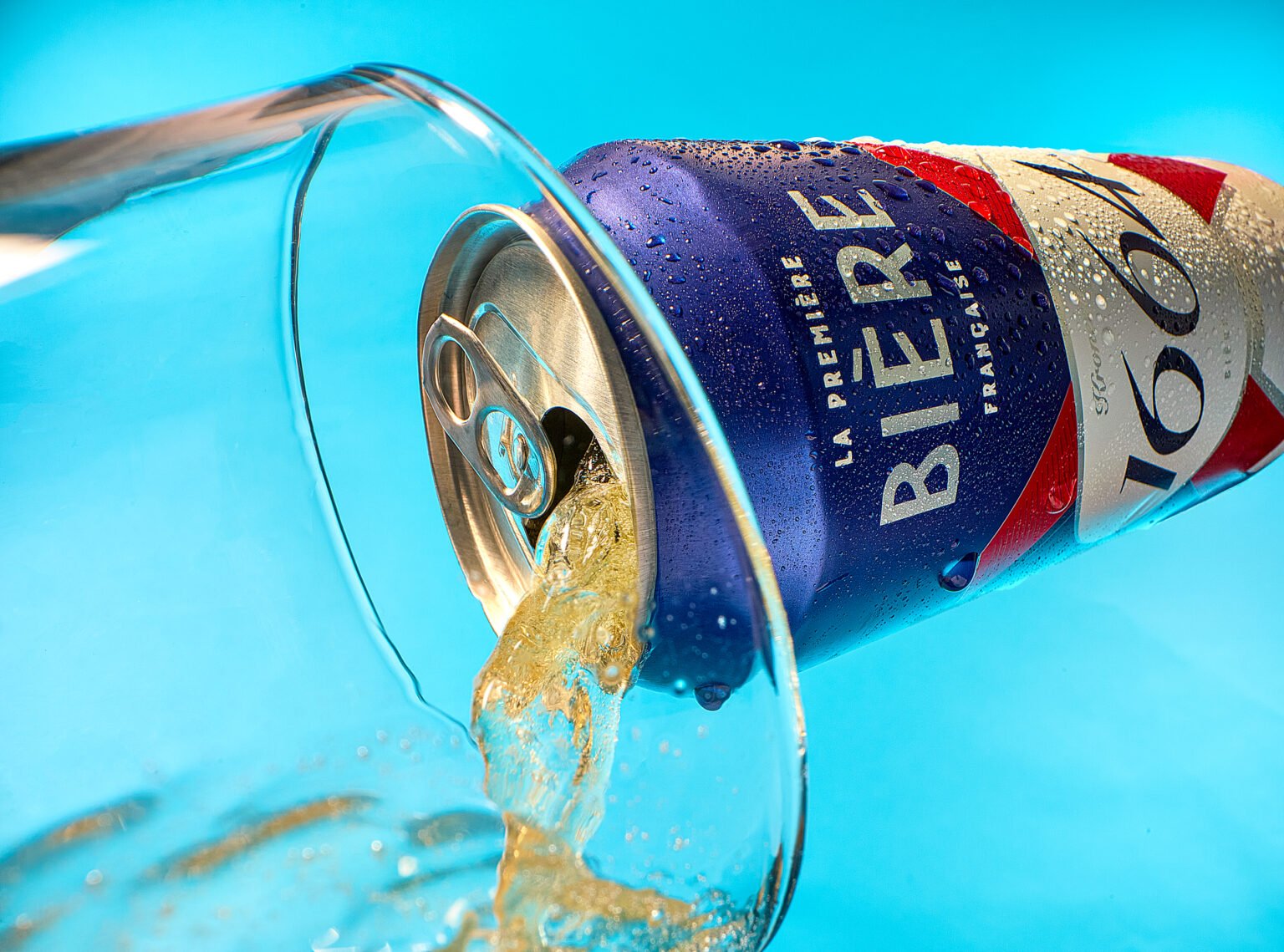 Chilled can labelled "La Première Bière Française" pouring beer into a glass against a bright blue background
