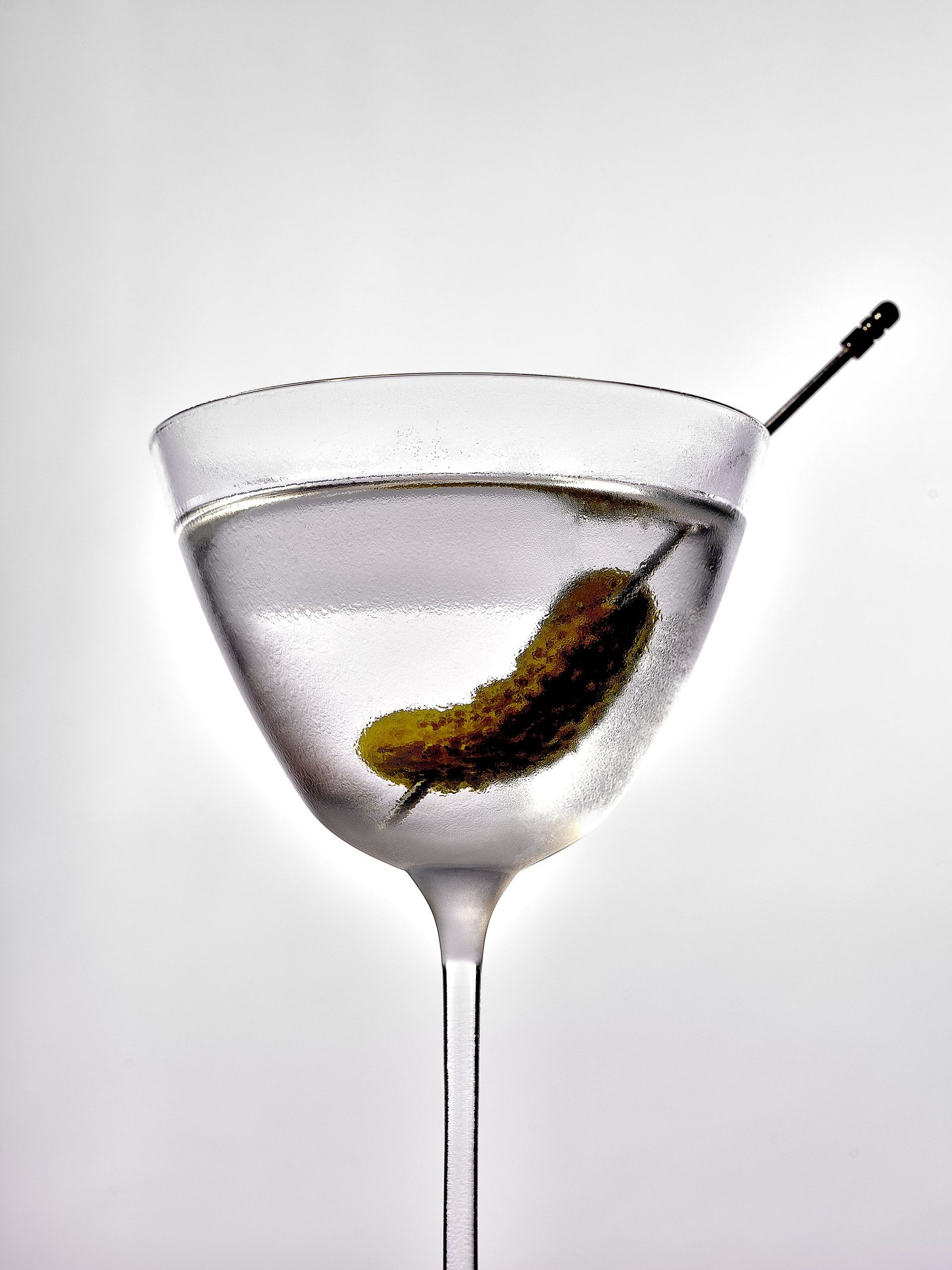 A martini glass with a clear cocktail garnished with a gherkin on a cocktail pick