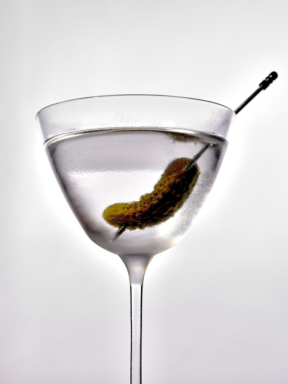 A martini in a stemmed glass, garnished with a pickled gherkin on a cocktail pick
